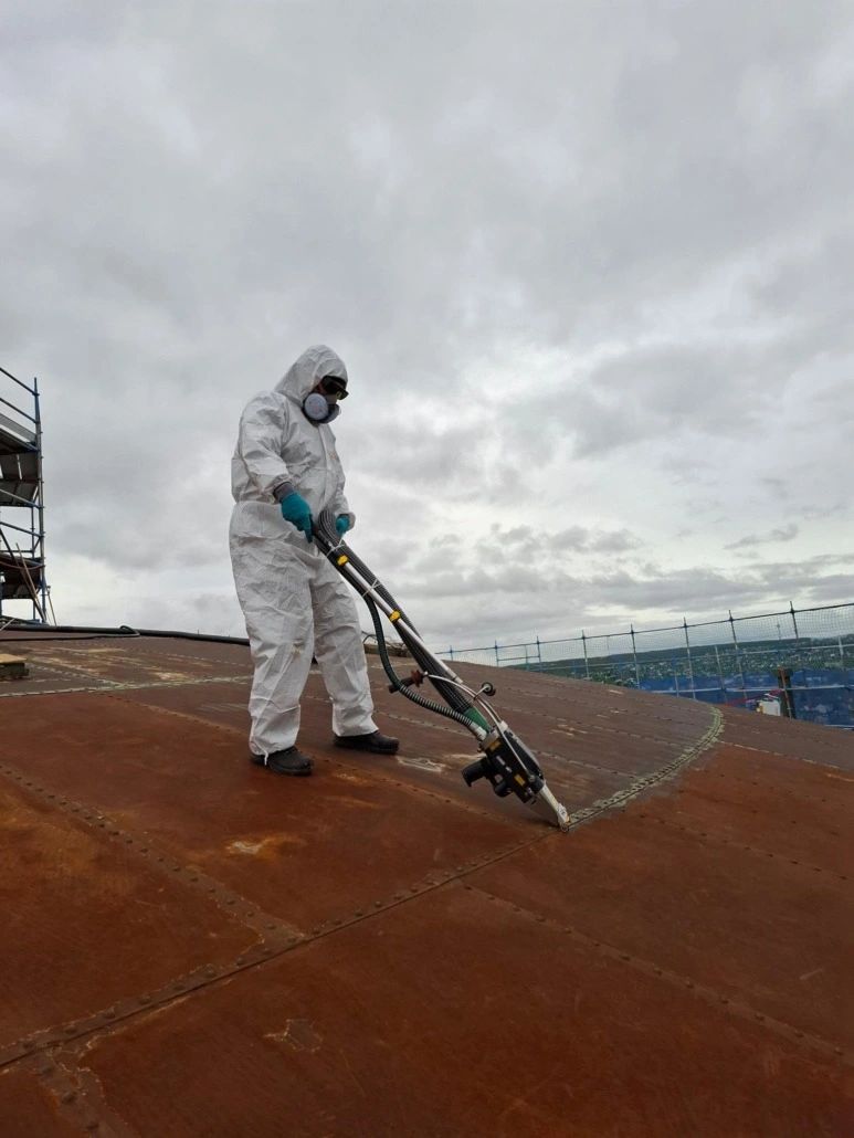 Operatore con tuta protettiva usa il CL500IM per la pulizia laser di uno scafo metallico