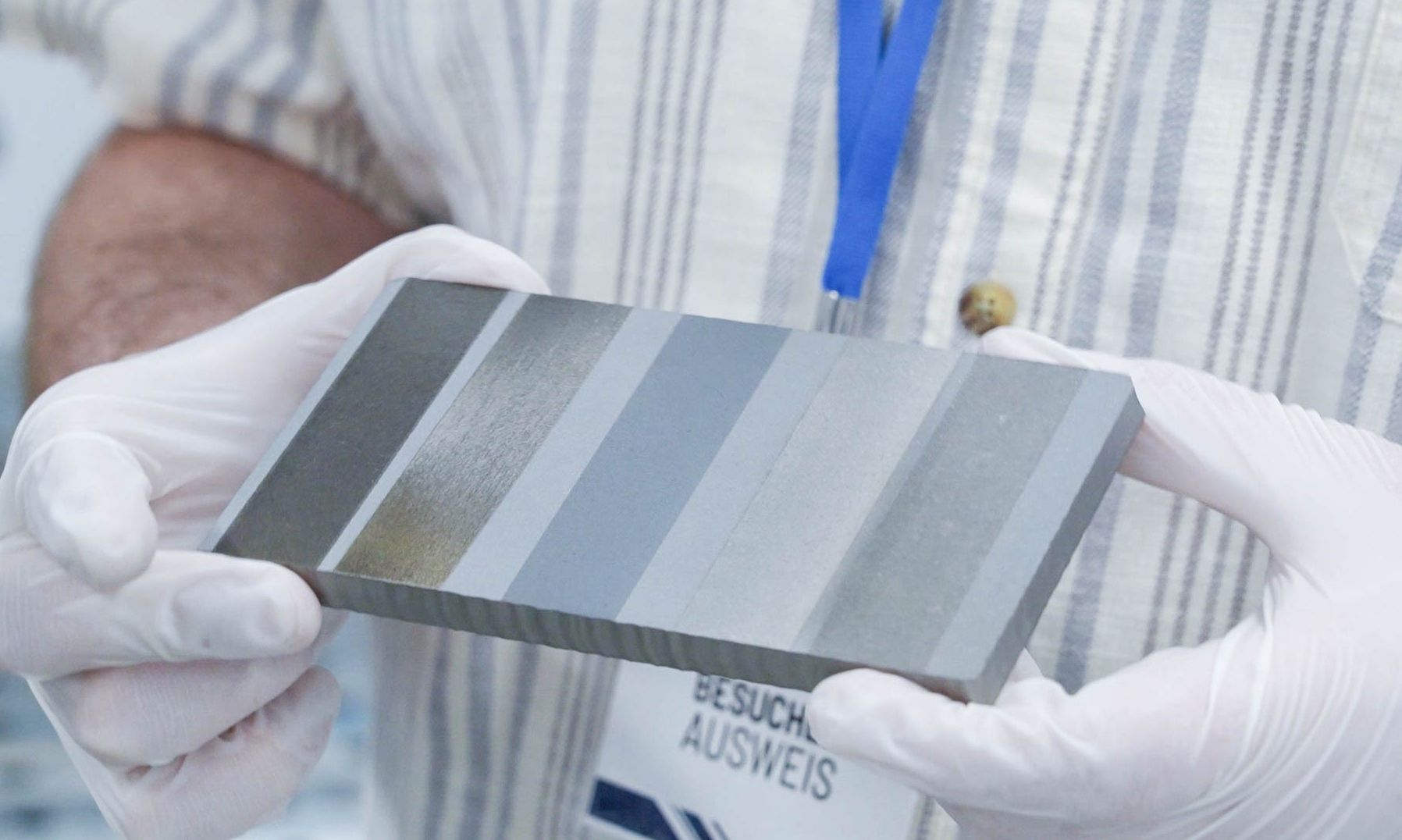 Tecnico con guanti bianchi regge campione metallico trattato a laser con strisce di ablazione progressive a diverse intensità
